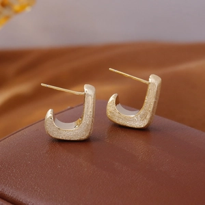 Orecchini geometrici vintage a forma di J in oro spazzolato su espositore in pelle