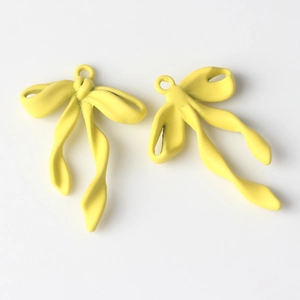 Detalle macro de par de colgantes de lazo en aleación amarillo brillante con cintas fluidas