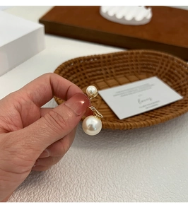 Primo piano di orecchini a doppia perla con perle grandi e piccole su stelo dorato