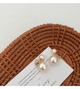 Dettaglio di eleganti orecchini a clip con doppia perla e base dorata su espositore testurizzato