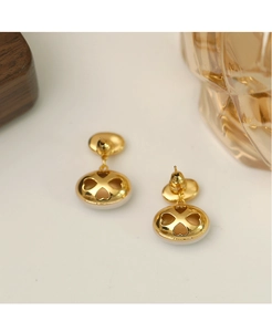 Vue macro de boucles d'oreilles ovales dorées avec trèfle en émail blanc ajouré