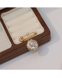 Detailed close-up of a vintage coin brooch with green enamel and pearl accents