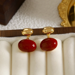 Boucles d'oreilles dorées avec pendentifs ovales rouges sur un écrin en velours crème