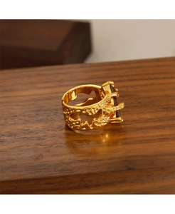 Detalle de anillo dorado con textura de lava y piedra rectangular sobre madera oscura