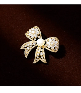 Macro detail of gold bow brooch featuring micro-pave zircons and a large freshwater pearl