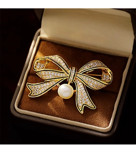 Macro detail of a golden vintage bow brooch with white crystals and large center pearl