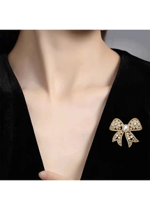 Detail of a gold bow brooch with sparkling cubic zirconia and a white freshwater pearl