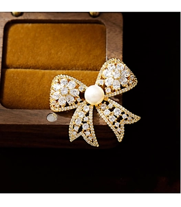 Close-up of golden bow brooch with zircons and pearl on vintage wooden box