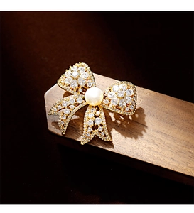 Detailed macro view of gold bow brooch with sparkling cubic zirconia and white freshwater pearl