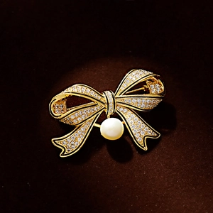 Vintage gold bow brooch with sparkling cubic zirconia and a white pearl on velvet