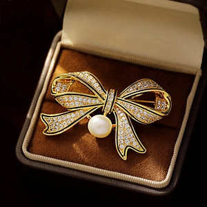 Vintage gold bow brooch with sparkling crystals and a large pearl in a jewelry box