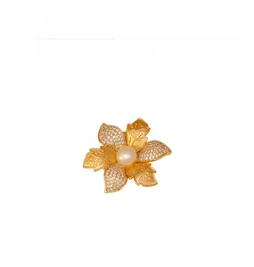 Détail macro d'une broche fleur avec perles, zircons et feuilles dorées texturées