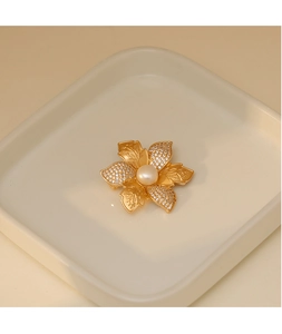 Détail d'une broche fleur vintage avec pétales dorés, zircons brillants et perle centrale