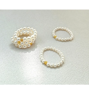 Detailed shot of elastic pearl rings set with golden geometric beads on gray surface