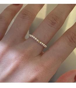 Macro detail of elastic pearl ring featuring small white pearls and a gold focal bead