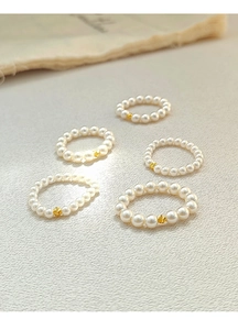 Detailed view of five handcrafted pearl rings with golden beads on white leather texture