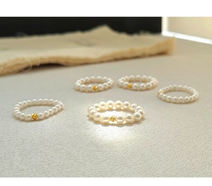 Detailed close-up of handmade pearl elastic rings with textured gold beads on beige linen