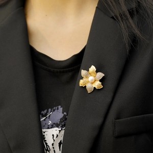 Broche fleur vintage avec pétales dorés, diamants blancs et perle sur veste noire