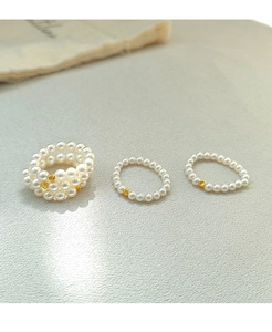 Detailed view of 3-piece handmade pearl ring set with gold metal beads on gray surface