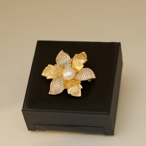 Broche fleur dorée élégante avec perle blanche et zircons sur boîte noire mate
