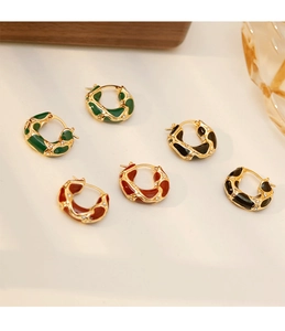 Détail de boucles d'oreilles émaillées vintage avec texture dorée en rouge, vert et noir