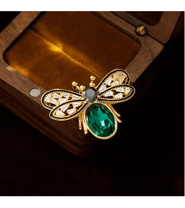 Close-up of golden bee brooch featuring a large oval emerald green stone and zircon wings