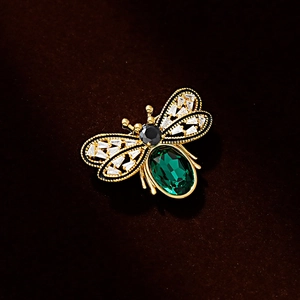 Elegant gold bee brooch featuring a large green gemstone and crystal-set wings