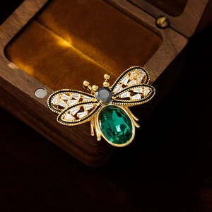 Elegant gold honey bee brooch with emerald gemstone and crystals on wooden jewelry box