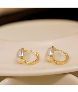 Close-up of gold-plated hoop earrings featuring translucent white round beads on ceramic
