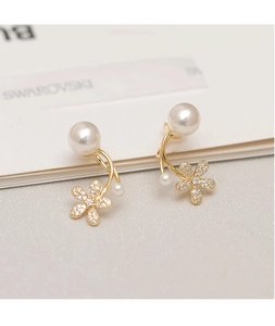 Dettaglio di eleganti orecchini a fiore dorati con perle e cristalli su sfondo bianco puro