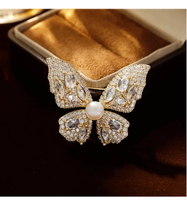 Makroaufnahme der Gold-Schmetterlingsbrosche mit Zirkonia und Perle auf braunem Samt