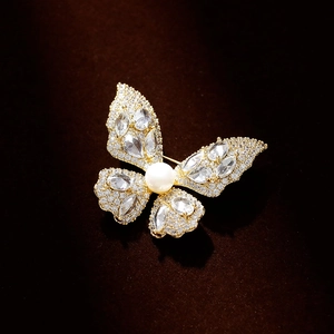 Eleganter Schmetterlings-Brosche in Gold mit weißer Perle und Kristallen auf Samt-Hintergrund