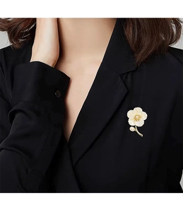 Détail d'une broche fleur avec pétales en nacre et centre en perle sur blazer noir