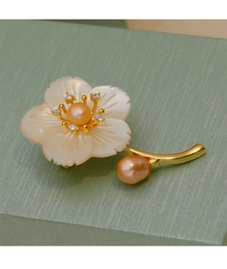 Détail d'une broche fleur en nacre avec perles roses sur un coffret vert clair