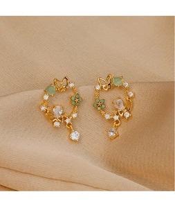 Detailed macro of gold flower earrings with green stones and crystals on silk