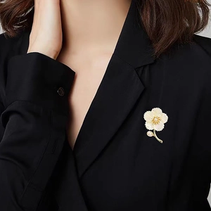 Broche fleur élégante avec pétales en nacre et accents dorés sur un blazer noir chic