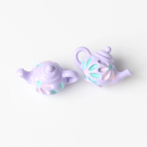 Macro view of mini purple teapot charms with embossed floral pattern for DIY jewelry