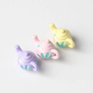 Three colorful miniature alloy teapots in purple, pink and yellow with floral texture