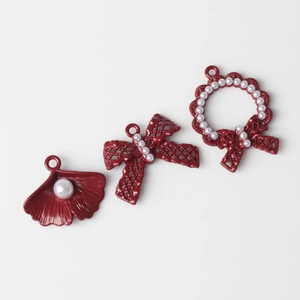 Macro shot of dark red enamel charms with pearls in ginkgo, bow, and wreath shapes