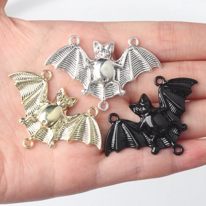 Three metal alloy bat connector charms in gold, silver, and black on a person's palm