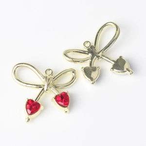 Detalle de colgantes de lazo con circón rojo y vista posterior de metal dorado