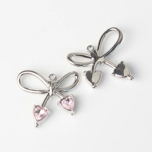 Detalle de colgantes de lazo con cristal de corazón rosa y base de metal plateado