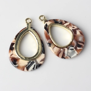 Detailed macro view of teardrop acetate resin charms with golden metal frames for DIY jewelry