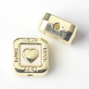 Close-up of golden square beads with LOVE engraving and heart motif for DIY jewelry