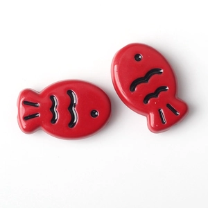 Dettaglio di piccole perline a forma di pesce smaltate rosse per gioielli fai-da-te