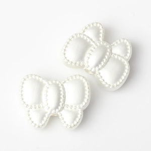 Detail view of two pearl white bow beads with beaded edges and threading holes for DIY