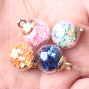 Handheld view of four colorful star-filled glass ball pendants for DIY jewelry making