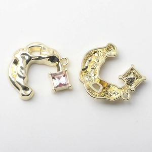 Macro detail of C-shaped alloy charms with pink rhinestones and gold plating for DIY jewelry