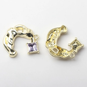 Detail of horseshoe-shaped gold metal pendant with purple gemstone and hanging loop