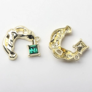 Detail of C-shaped golden pendant with emerald zircon and fluid lava texture